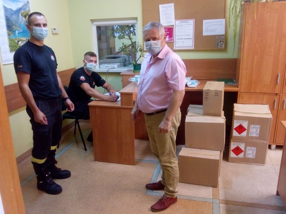 Zdjęcie przedstawia przedstawicieli Państwowej Straży Pożarnej i Urzędu Gminy Paprotnia i otrzymane środki ochrony osobistej przeciwko COVID 19